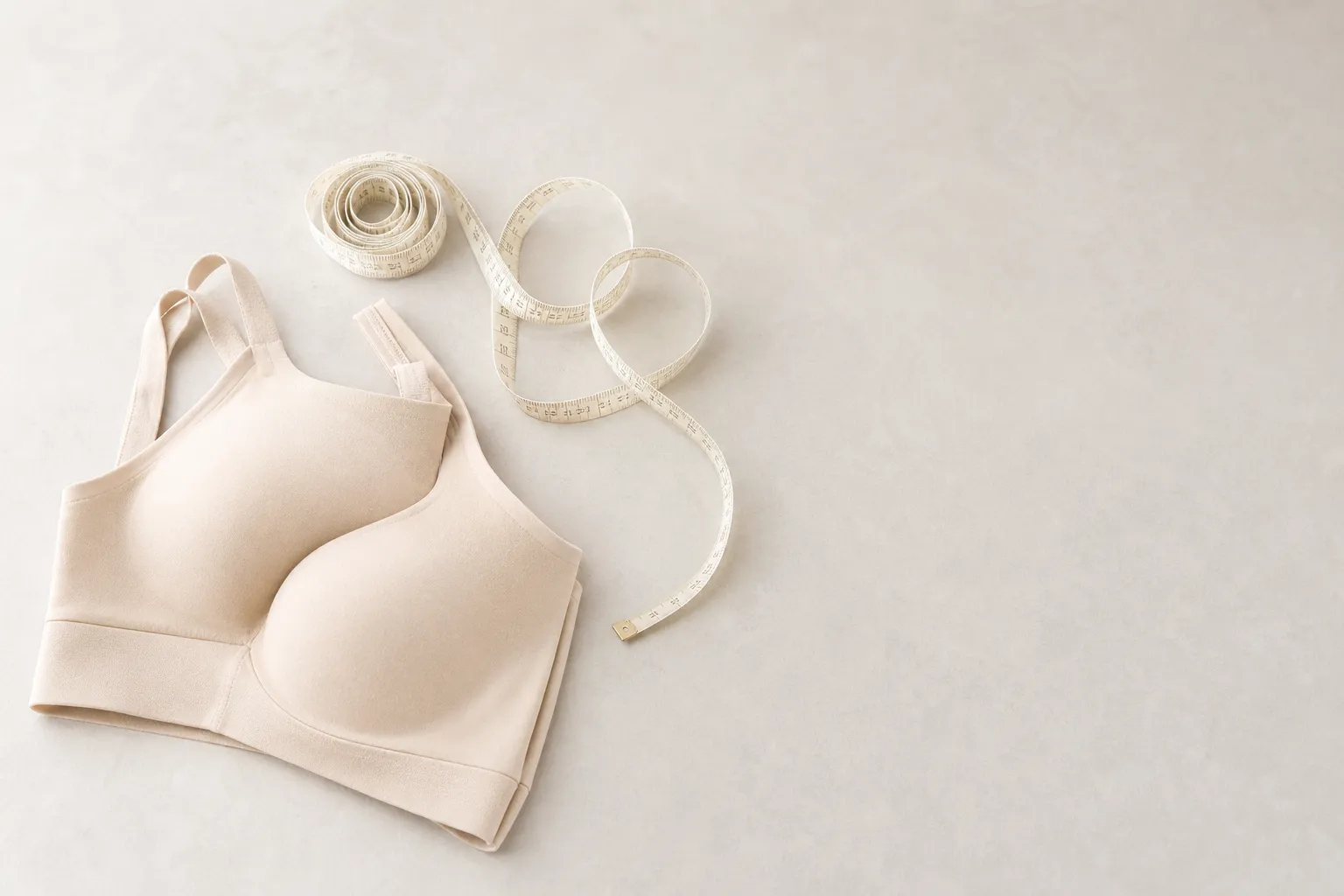 A soft measuring tape coiled beside neatly folded lingerie on a light surface