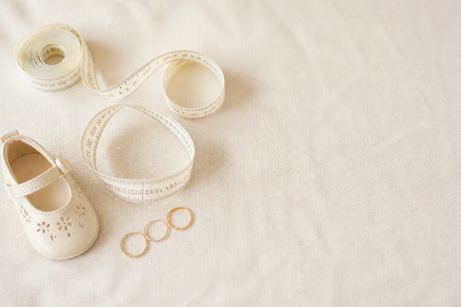 A soft tape measure, a small shoe and three rings arranged on light linen — size conversion made simple